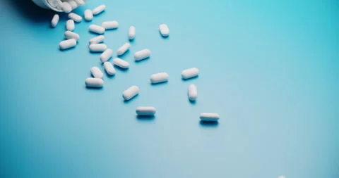 Spilling pills from white bottle on blue background - slow motion Vídeo Stock 307948785