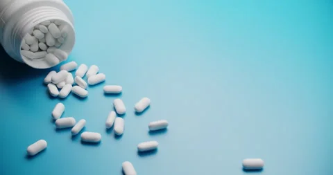 Spilling pills from white bottle on blue background - slow motion Vidéo 307948857