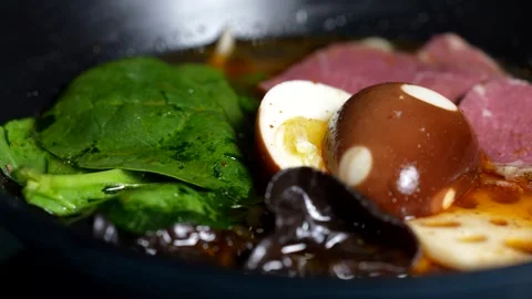 Spinach leaves, soy-marinated egg, mushrooms, and beef slices floating in rich  Stock Footage 313880822
