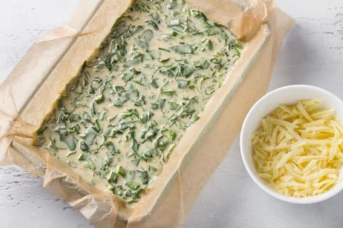 Spinach sorrel pie dough in a baking dish with parchment, a bowl of grated Photos
