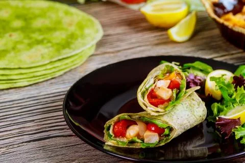 Spinach wrap with meat and vegetables on black plate with green salad. Stock Photos