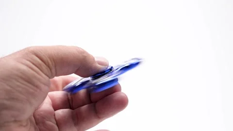 The spinning blue fidget spinner is held horizontally between two fingers. Stock Footage 313053979