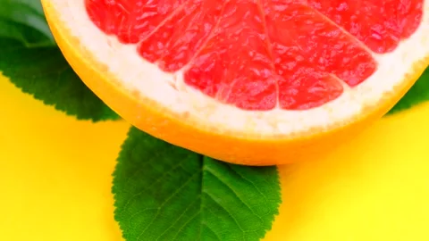 Spinning cut in half grapefruit with green leaves on yellow background Stock Footage 155700388