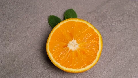 Spinning ripe orange, half with mint leaves on concrete gray background Stock Footage 154631523