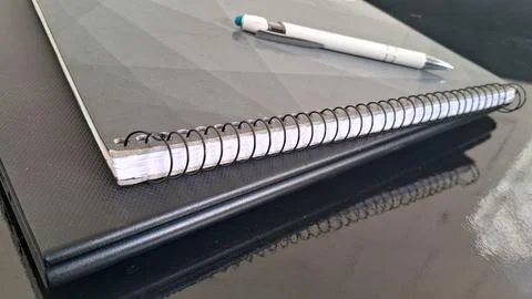 Spiral bound gray notebook with white pen on dark surface Stock Photos