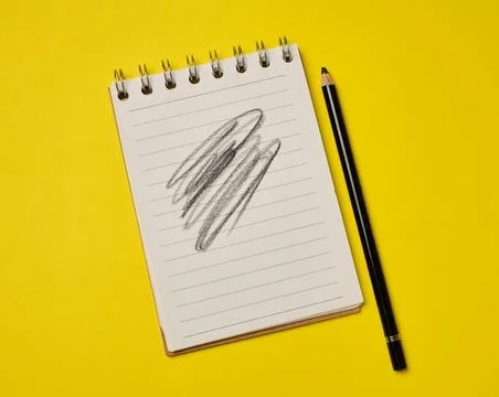 Spiral-bound lined notepad with a black pencil and a scribbled drawing on a.. Fotos Stock