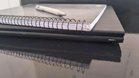 Spiral bound notebook with a white pen on black laptop Stock Photos