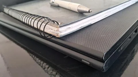 Spiral bound notebook with a white pen resting on laptop Stock Photos