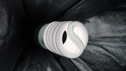 Spiral CFL bulb close-up on black textured fabric, minimal studio still life Stock Footage 331487841