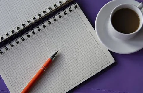 Spiral notepad in a cage on a lilac background with a cup of coffee Stock Photos