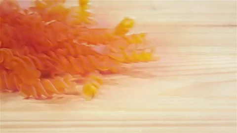 Spiral shape red pasta falls on wooden table, slow motion Stock Footage 75489629