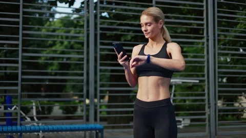 Spirited lady looking at cellphone with smartwatch to analyze workout activity Stock Footage 252198336