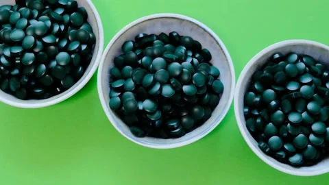 Spirulina pills in three cups on a green background.Rotation. Stock Footage 156552811