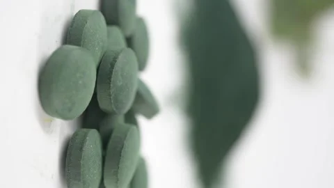 Spirulina pills on white surface with green leaves in background showing or.. Stock Footage 332744855