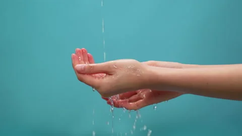 Splash of clean water flows into the hands on the blue background. 스톡 동영상 153962559