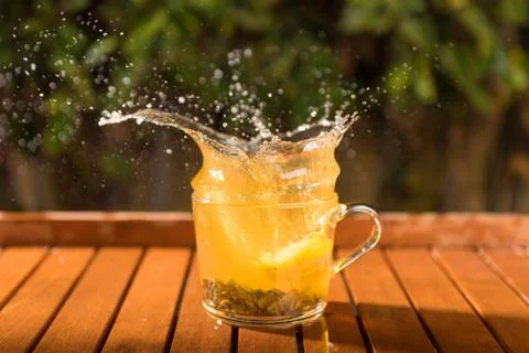 Splash of cool fresh tea with lemon in the transparent glass cup in the table Stock Photos