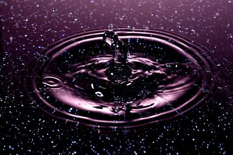 Splash - a drop falling onto the water surface in a color macro shot Stock Photos