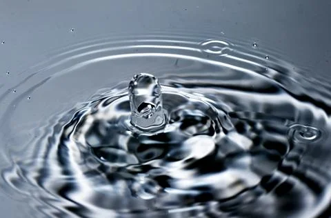 Splash - a drop falling onto the water surface in a color macro shot Stock Photos