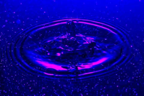 Splash - a drop falling onto the water surface in a color macro shot Stock Photos