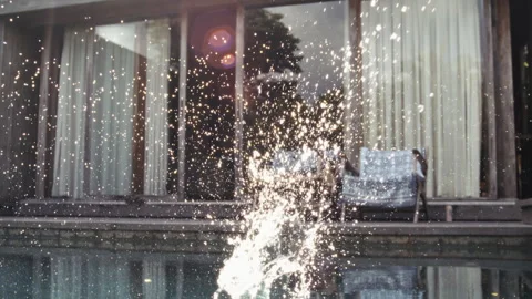 Splash Explodes in Sunlit Pool in Front of Lounge Chairs at Tropical Villa Stock Footage 316377346