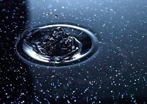 Splash - a falling drop of water breaking on the water surface Stock Photos