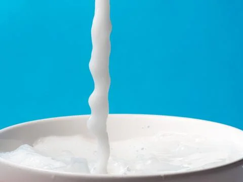 Splash of milk from a cup on blue background. Stock Photos