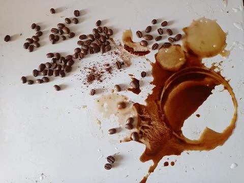 Splashes and drops of spilled coffee and coffee beans on a white table Stock Photos