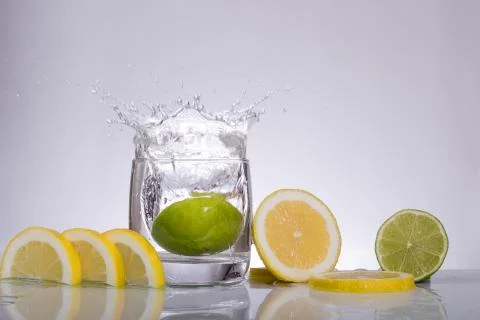 Splashes of water, lemon lime falling into a glass, isolated, reflection, whi Stock Photos