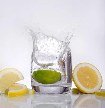 Splashes of water, lemon lime falling into a glass, isolated, reflection, whi Stock Photos
