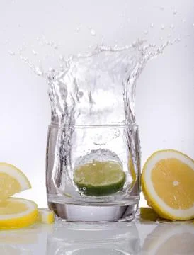 Splashes of water, lemon lime falling into a glass, isolated, reflection, whi Stock Photos