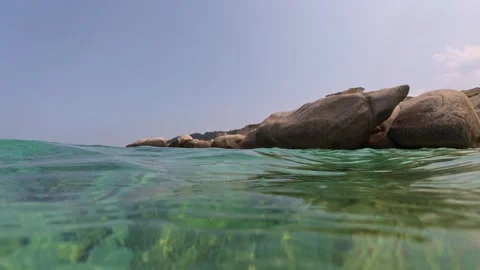 Split-level view of crystal-clear sea with large coastal rocks above and Stock Footage 313842279