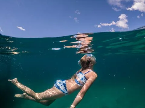 Split Level View of Young Girl Swimming Underwater in Lake Beneath Sky Foto stock