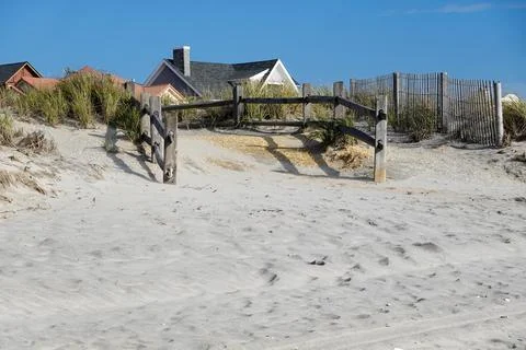 Split rail fence lining a pathway over sand dunes and high grass entering a w Stock Photos