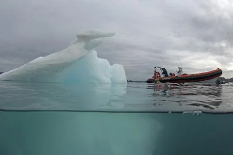 Split shot of and iceberg with a rubber boat close to it Stock Photos