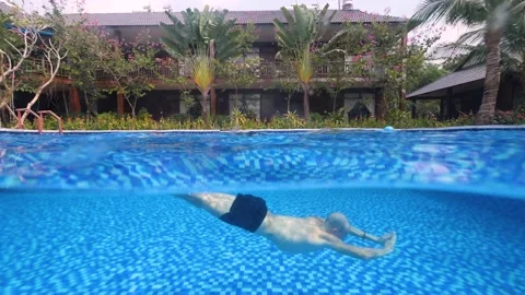 Split underwater shot of a man swimming in the pool on a summer day in a resort. Stock Footage 172462803