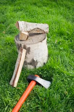 Splitting axe lying on the grass and nearby birch firewood Stock Photos