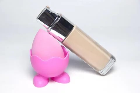 Sponge for the base. Pink sponge for makeup. Bottles of foundation Foto stock