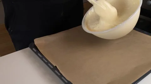 Sponge cake batter being poured from a mixing bowl onto parchment paper on a Stock Footage 317154663