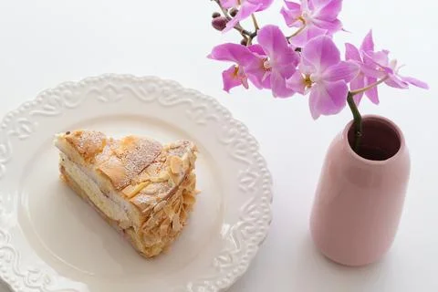 Sponge cake on a white plate on the table. There is a vase with a flower on.. Stock Photos