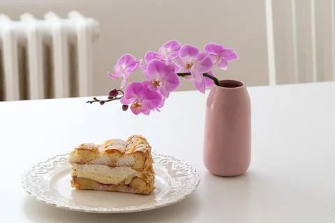 Sponge cake on a white plate on the table. There is a vase with a flower on.. Stock Photos