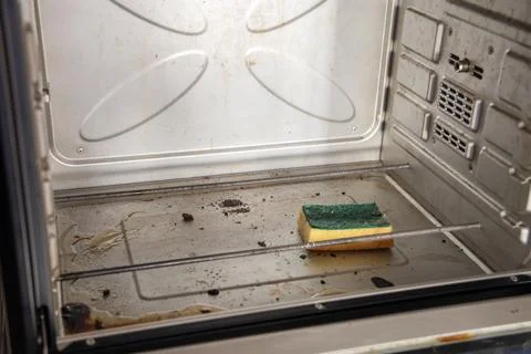 Sponge with cleaning solution lies in dirty oven with burnt grease stains on the Stock Photos
