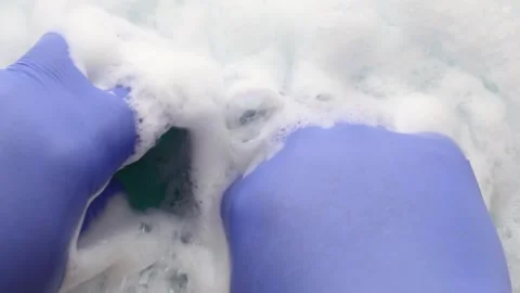 A sponge soaked in soapy water forms a foam. Hands in blue gloves Stock Footage 279343216