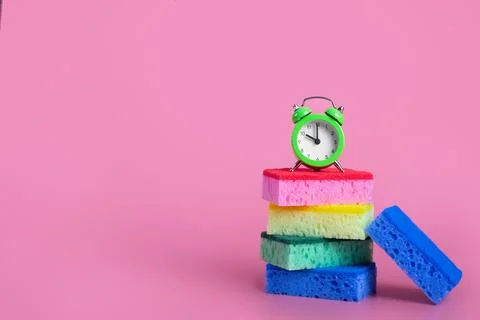 Sponges multi colored with alarm clock on isolated pink background cleaning c Stock Photos