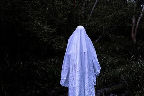 A spooky ghost, covered in a white sheet. Standing in a scary dark haunted f.. Stock Photos