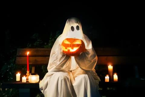 Spooky ghost holding a glowing pumpkin in the dark night. A lit candle adds.. Stock Photos