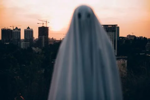 Spooky ghost standing against evening city during Halloween Stock Photos