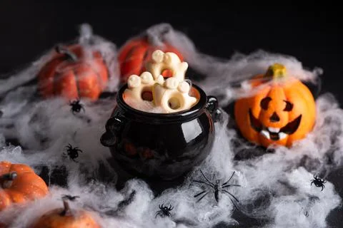Spooky Halloween cauldron filled with ghost shaped cookies surrounded by pu.. Stock Photos