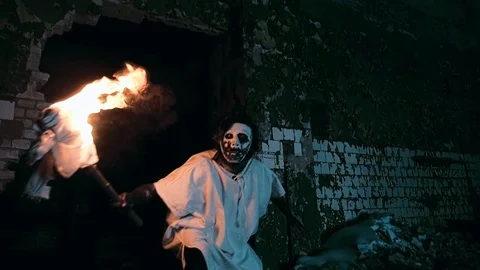 Spooky psycho in a mask with a torch coming out of a hole in a wall Video stock 92178690