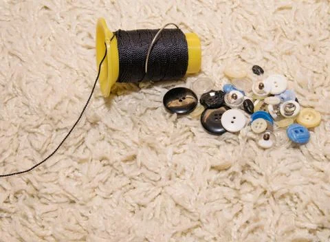 A spool of black strong thread and a bunch of buttons lie on a white backgrou Stock Photos