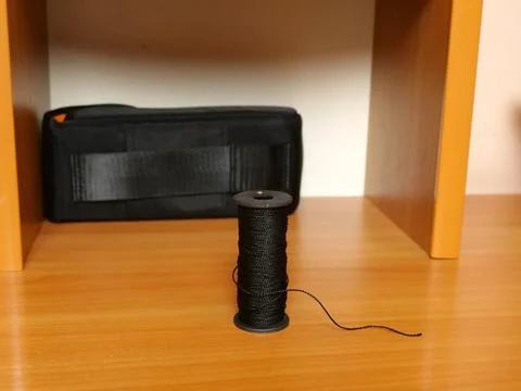 Spool of black thread standing upright on wooden shelf with soft background. Stock Photos